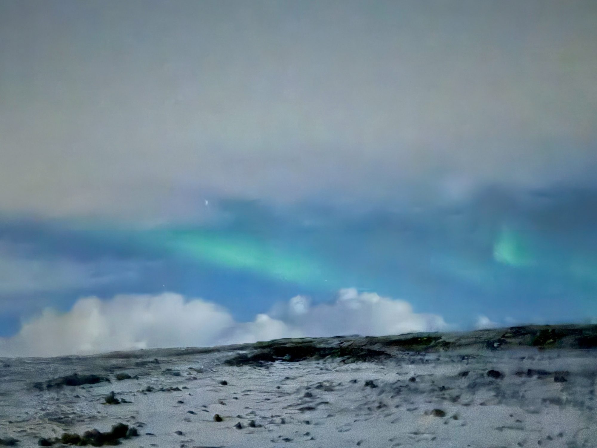 A faint green ribbon of the aurora over a snow-covered Icelandic landscape