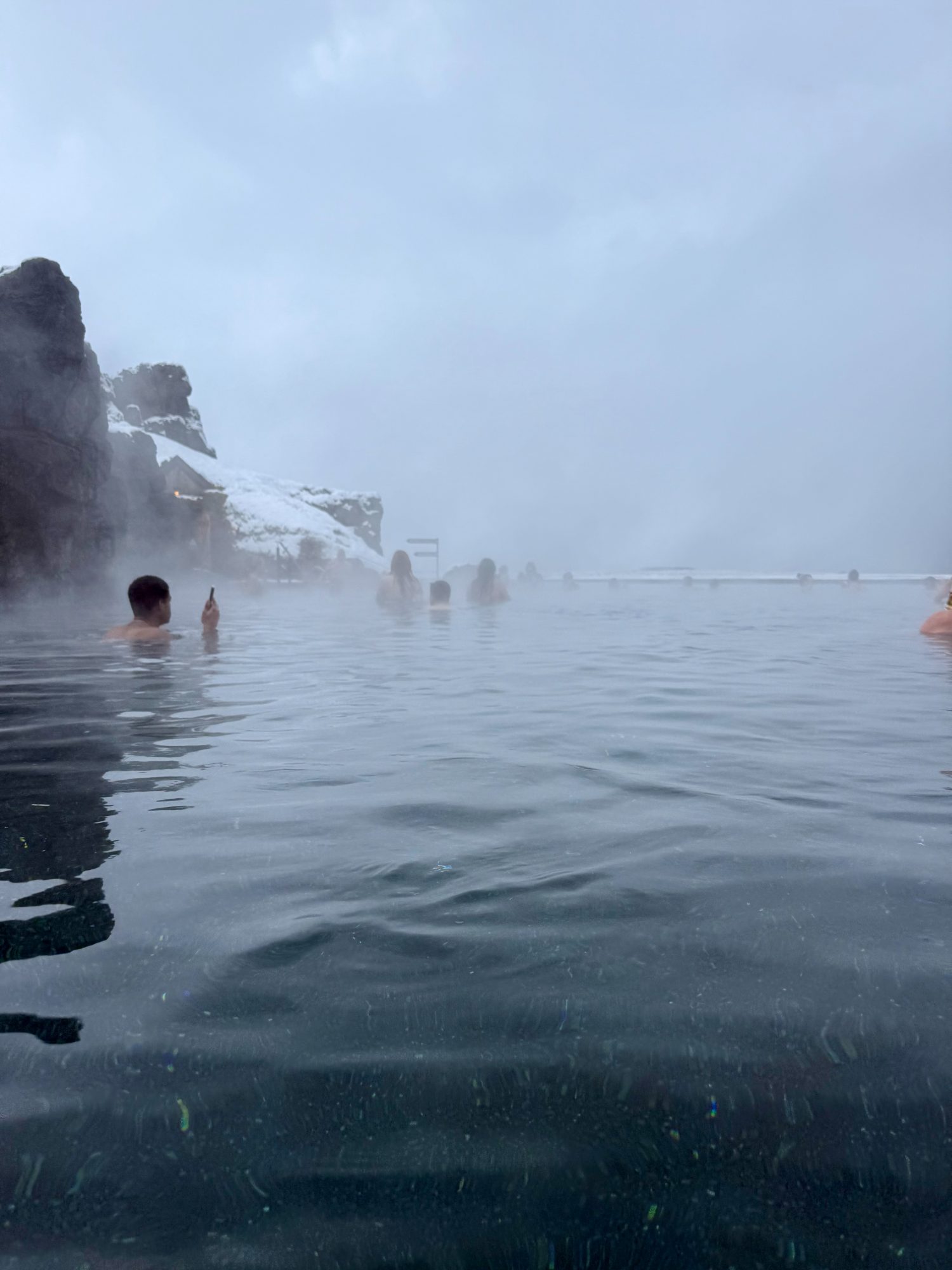 Bathers in the steaming geothermal water of the Sky Lagoon beneath snow-dusted cliffs