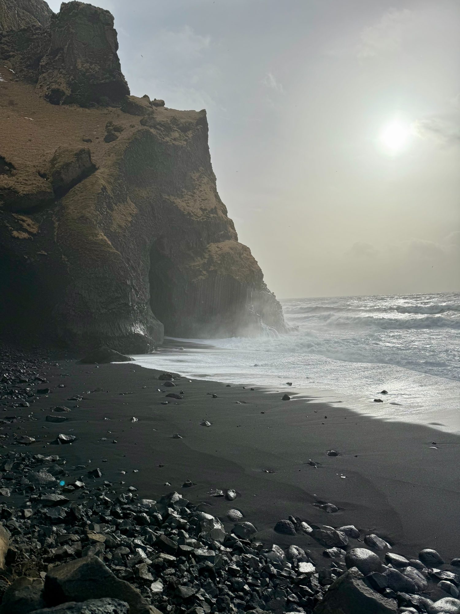 Waves meeting a black-sand beach beneath Icelandic sea cliffs