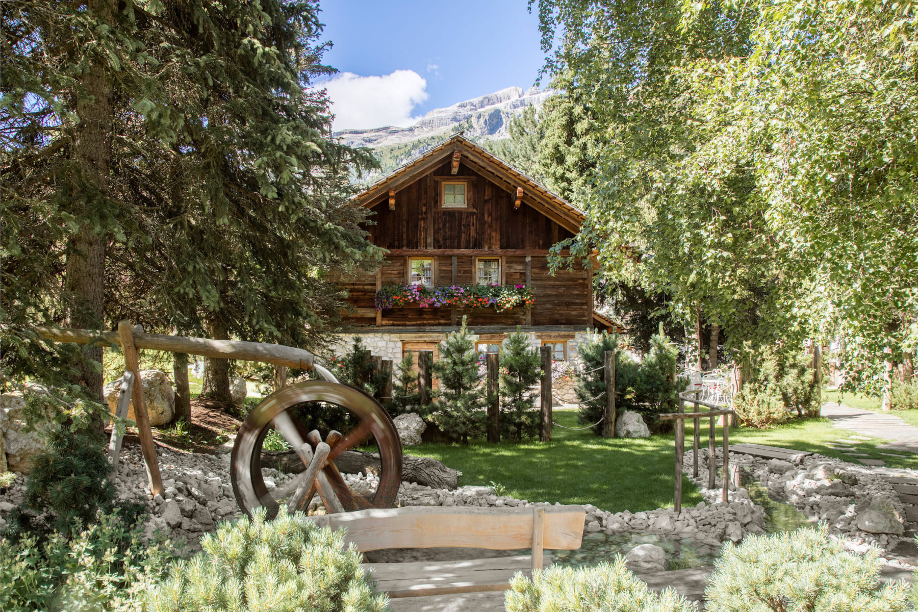 A traditional Ladin chalet and water wheel in the gardens at Hotel La Perla